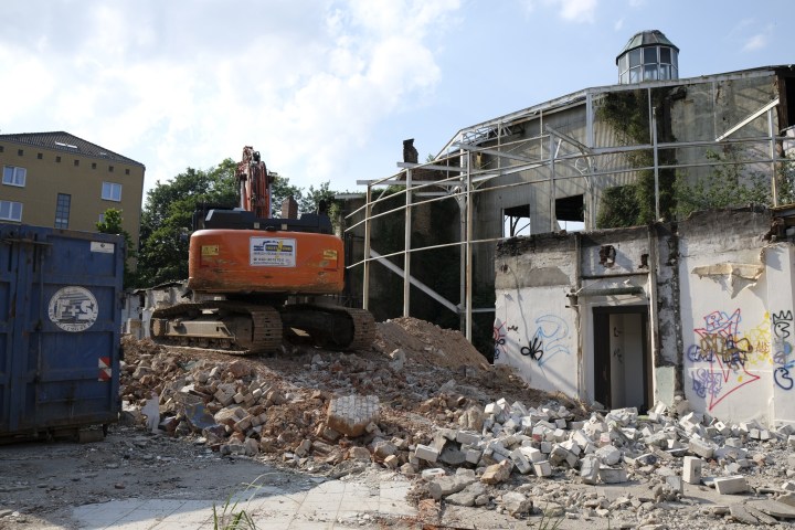 Excavator and debris at demolition site with a partially demolished building.