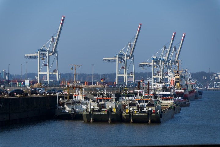 Port scene with cargo ships and cranes under a clear blue sky.