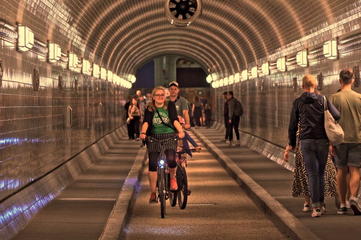 A cyclist and pedestrians in a well-lit tiled tunnel.