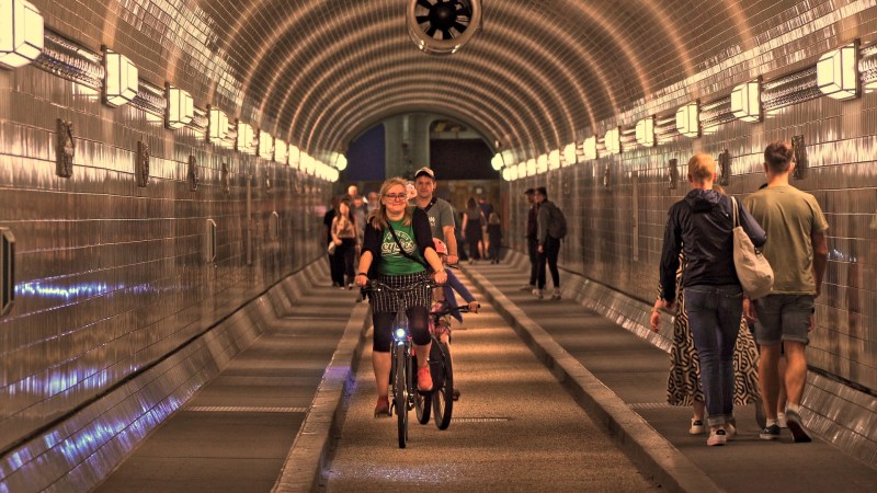 A cyclist and pedestrians in a well-lit tiled tunnel.