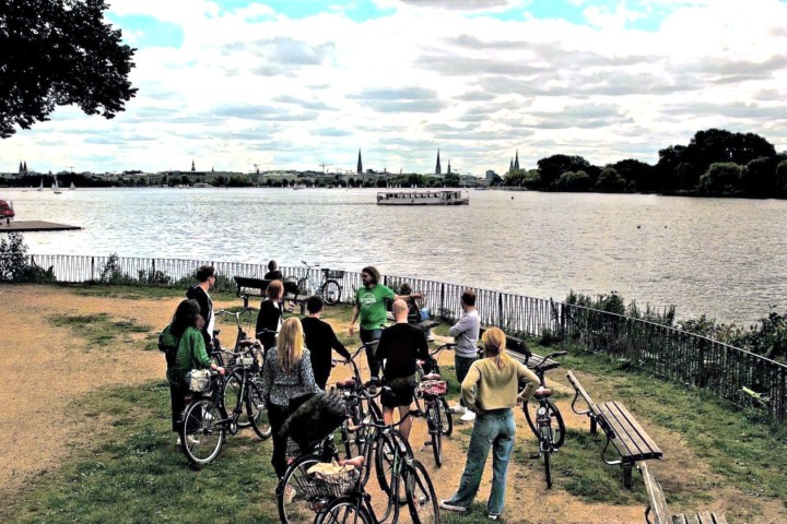 Group of people with bicycles by a lake under a cloudy sky.