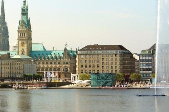 City skyline with historic buildings and fountain by a lake.