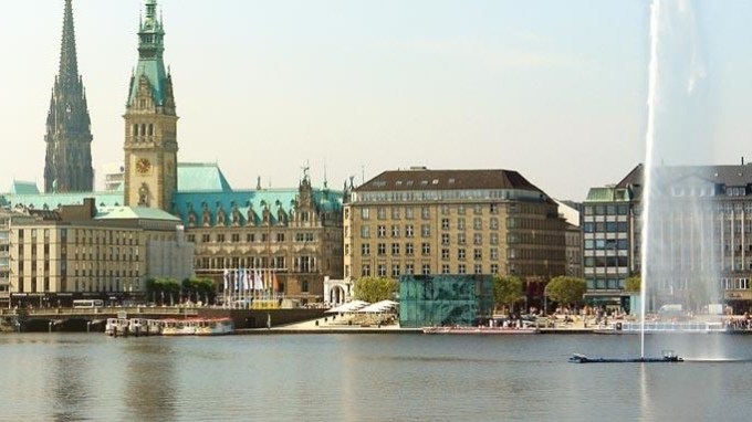 City skyline with historic buildings and fountain by a lake.