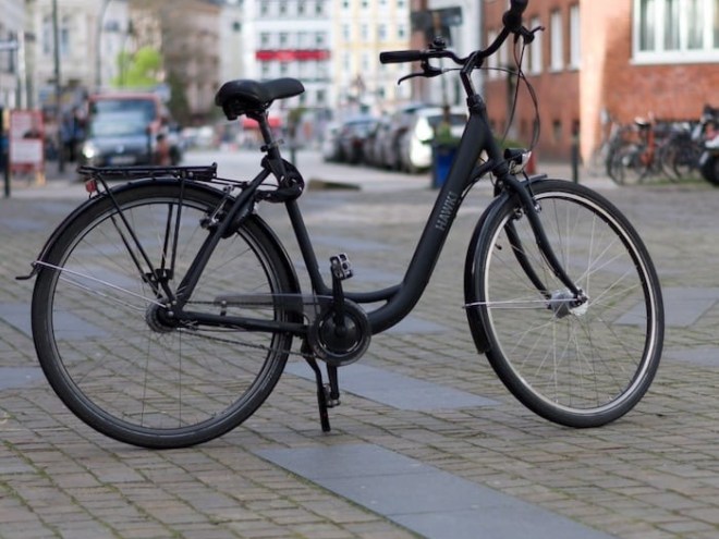 Black bicycle on cobblestone street in urban setting with buildings.