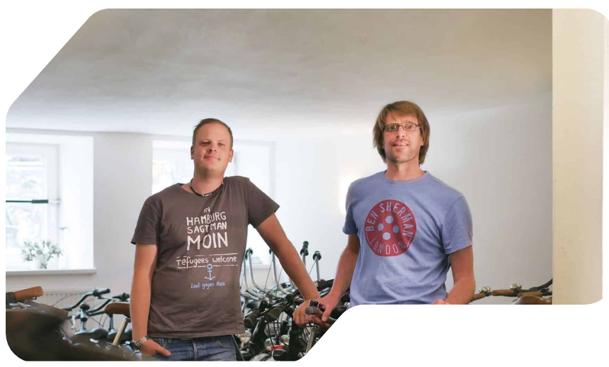 Two people in a room with white walls and bicycles in the background.