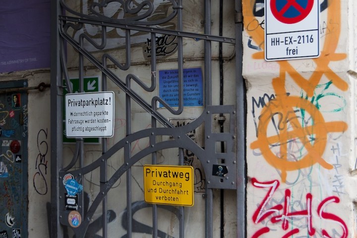 Graffiti-covered metal gate with various warning and parking signs.